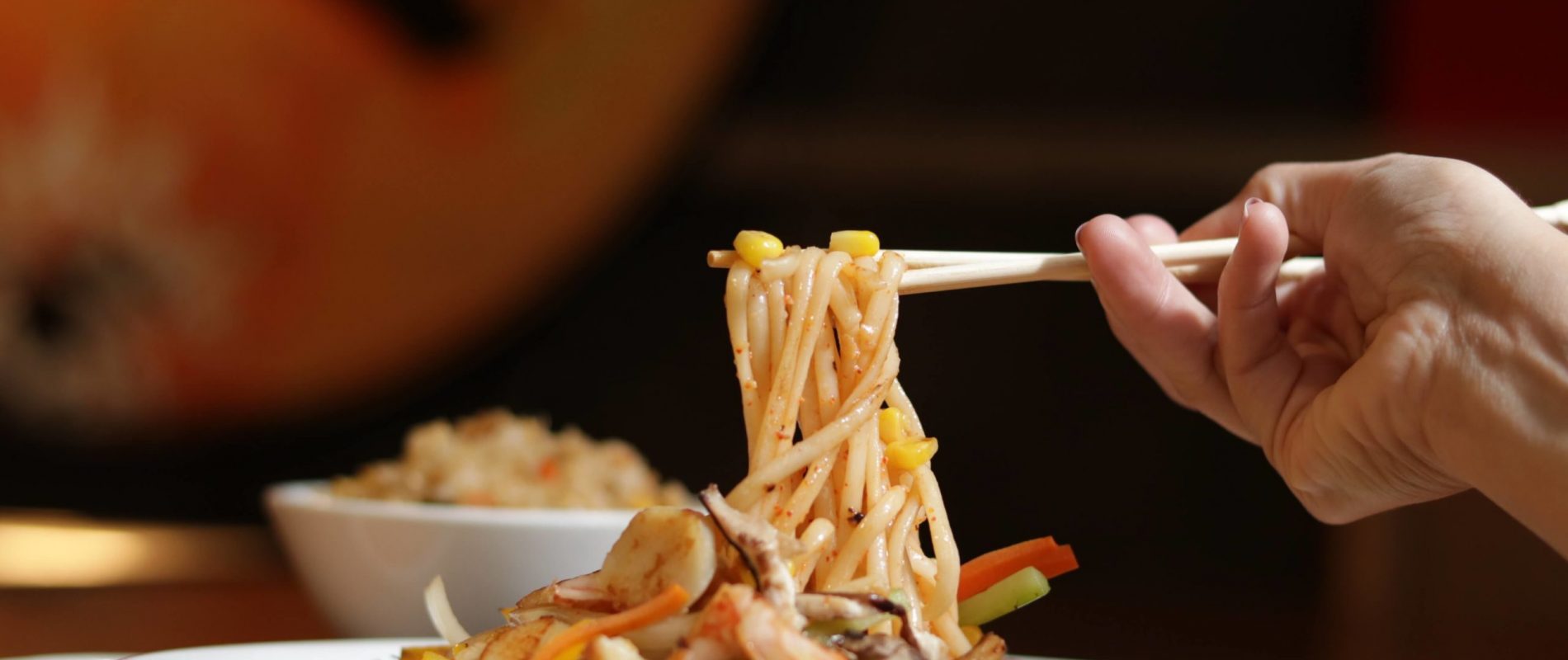 Noodles with corn being picked up by a hand with chopsticks
